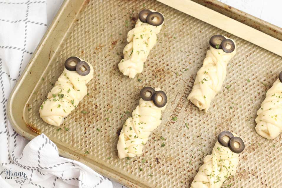 Add seasoning to your Halloween breadsticks and place olive eyes on top to finish making your Halloween finger foods