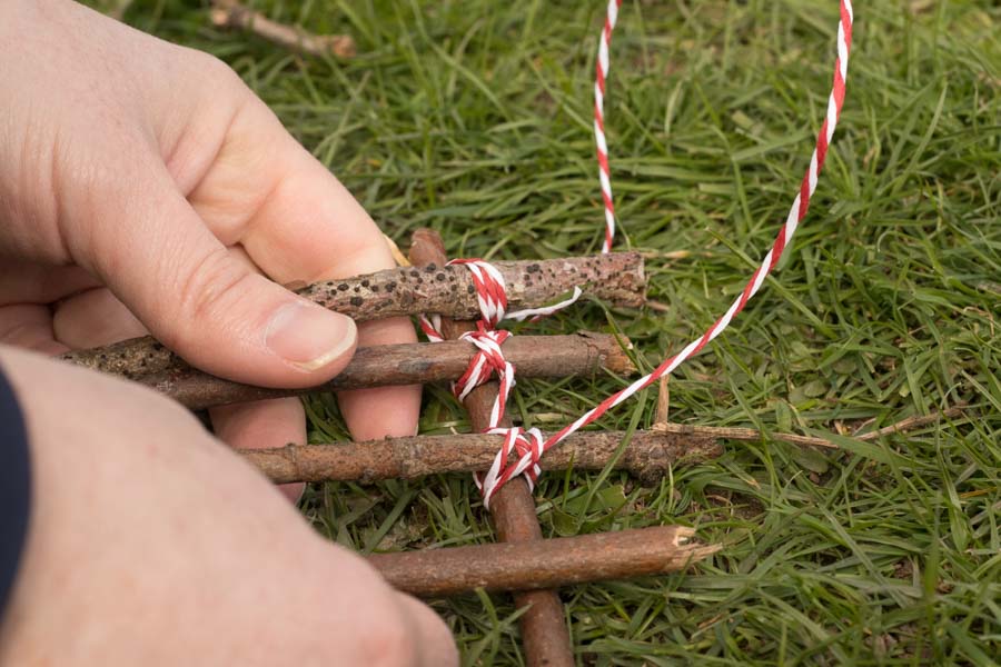 Hands folding a stick raft together as yarn is wrapped around to tie it together
